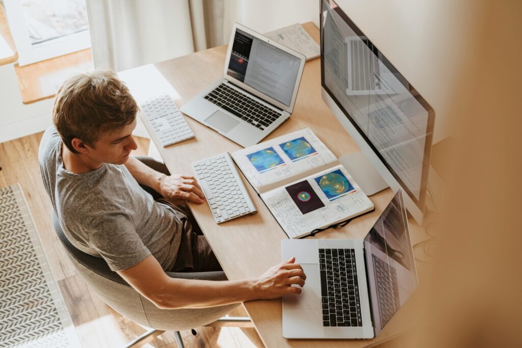 Freelancer working at a desk with multiple laptops and notebooks, representing the typical work setup of online freelancers on platforms like Upwork and Fiverr.